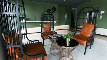 A modern lounge area with metal chairs and a central coffee table, green walls, and a white floor.