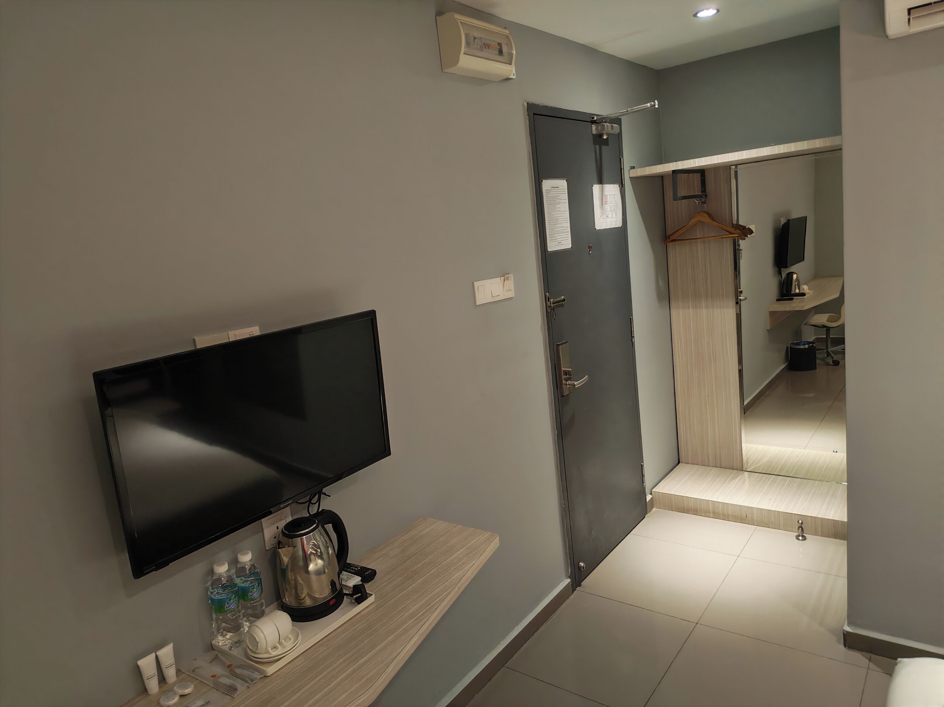Habitación de hotel con televisión de pantalla plana, un banco de madera, un hervidor de agua y artículos de aseo.