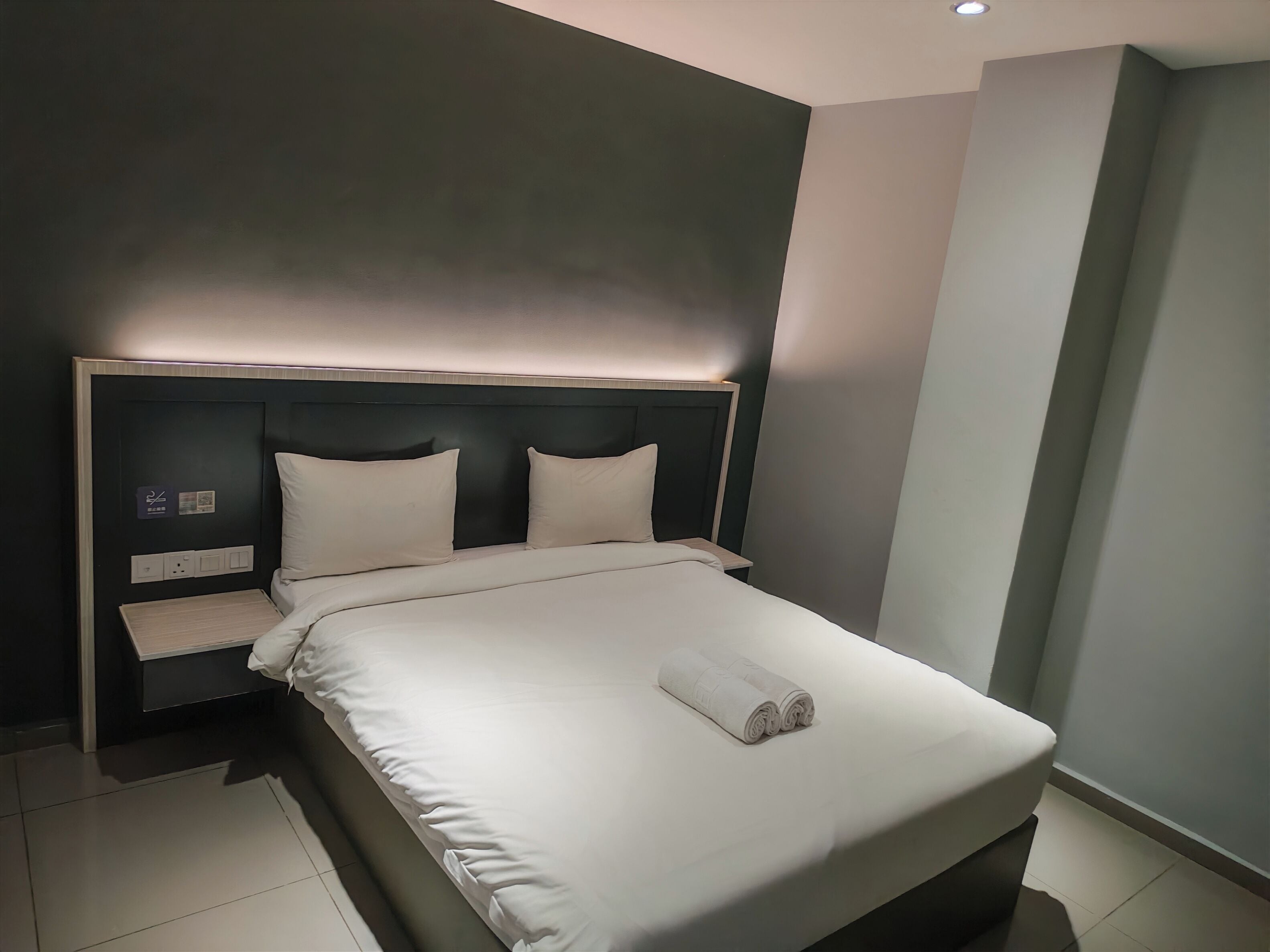 A modern hotel room with a bed, bedside tables, and a headboard.