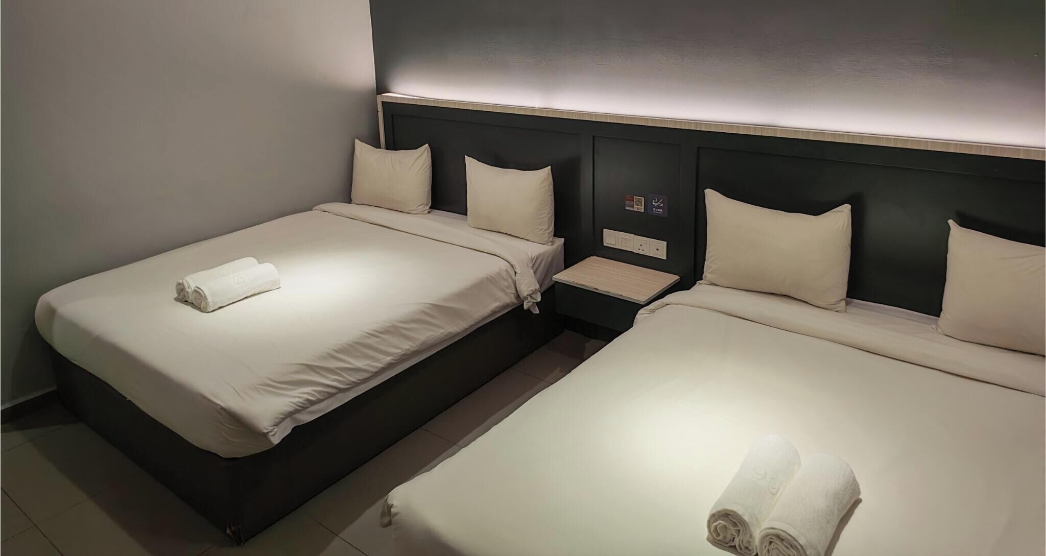 A hotel room with two beds, each with a pillow and a rolled towel.