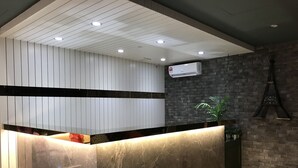Bancada de recepção com superfície de mármore, painel de parede branco, parede de tijolos e um relógio.
