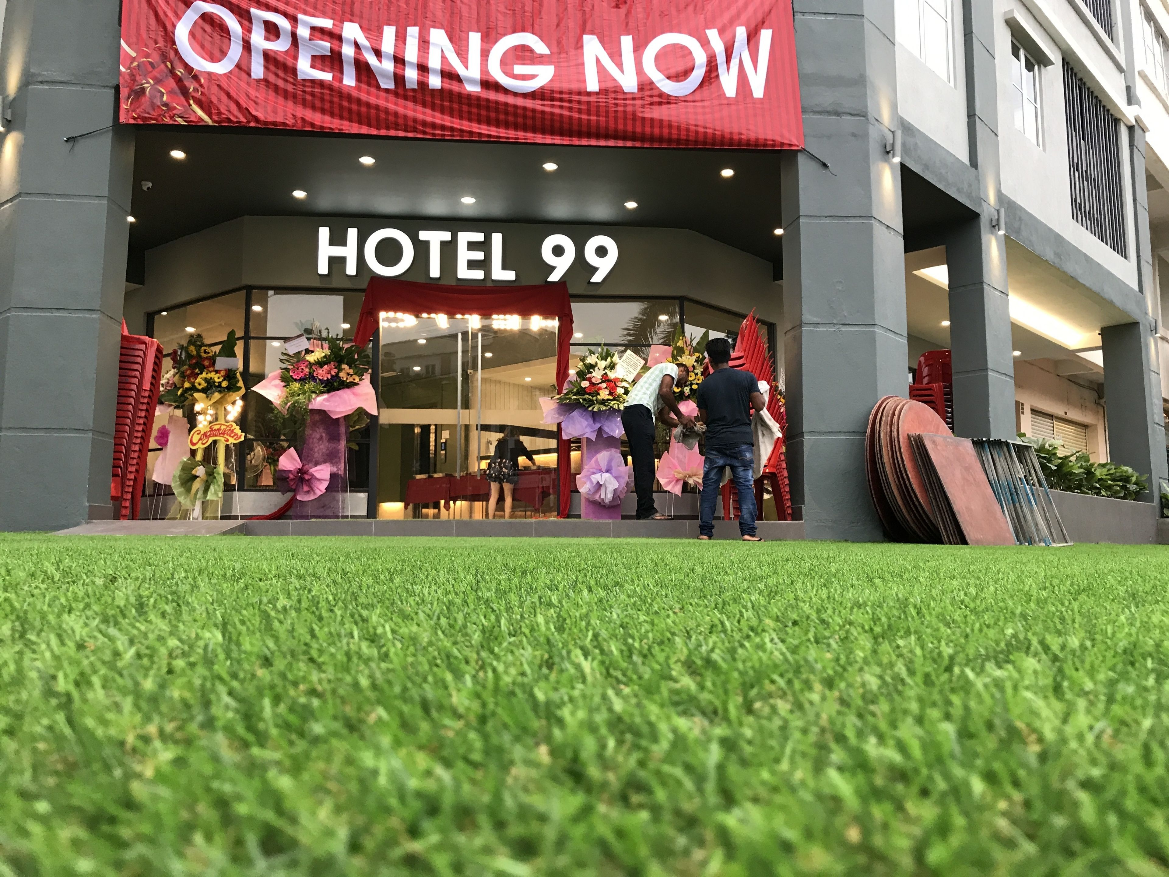 A hotel entrance with a red banner stating "OPENING NOW" and the name "HOTEL 99".