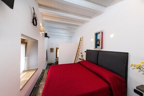 A bedroom with a bed, a ladder, a painting, and a small table with a vase of flowers. - La Quercia e l'Asino (Piazza Armerina)