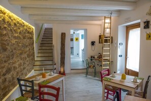 A dining area with a rustic stone wall, wooden staircase, and a view into a kitchen area. - La Quercia e l'Asino (Piazza Armerina)
