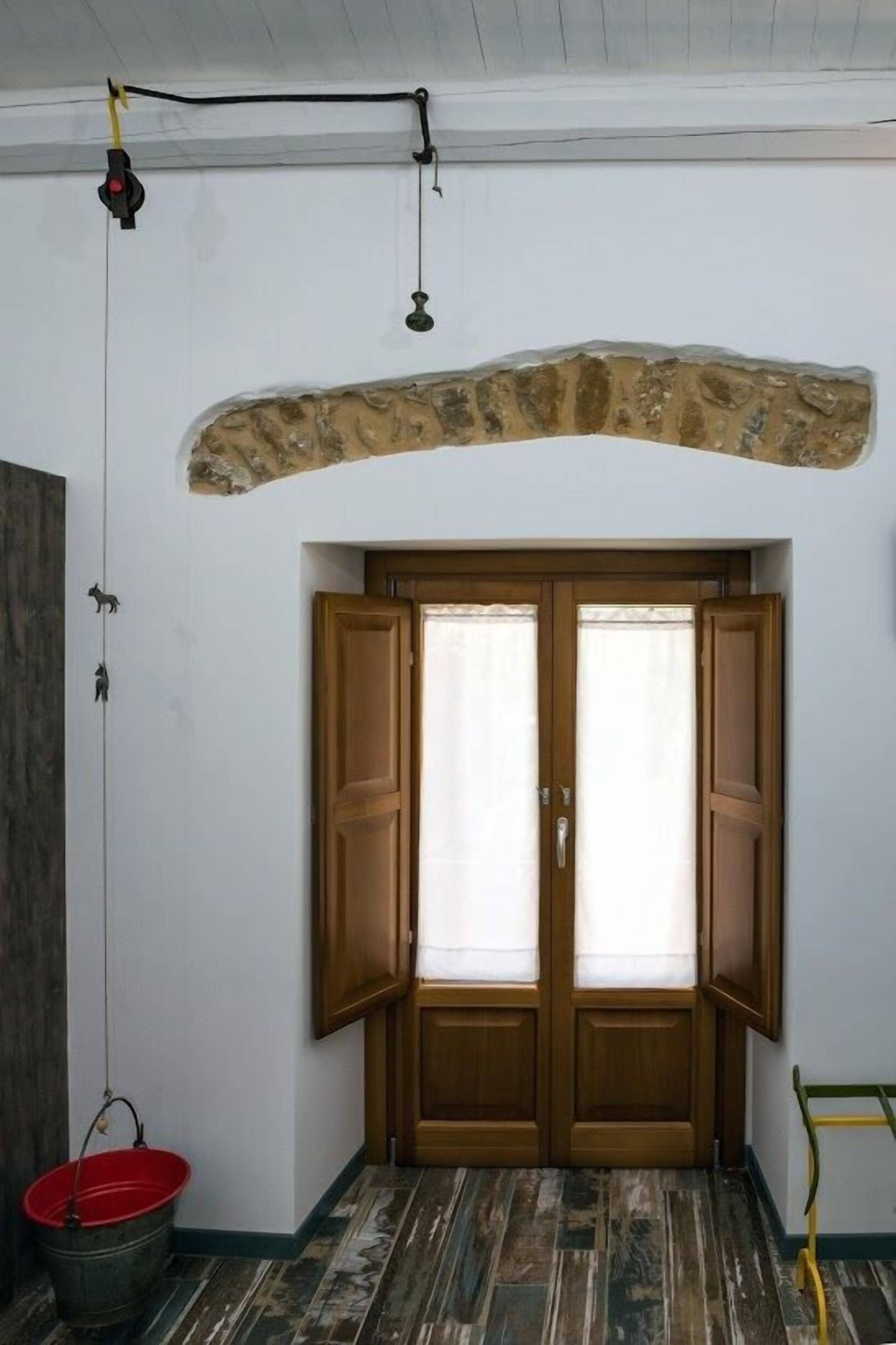 A room with a stone archway, wooden double doors, a red bucket, and a yellow ladder.