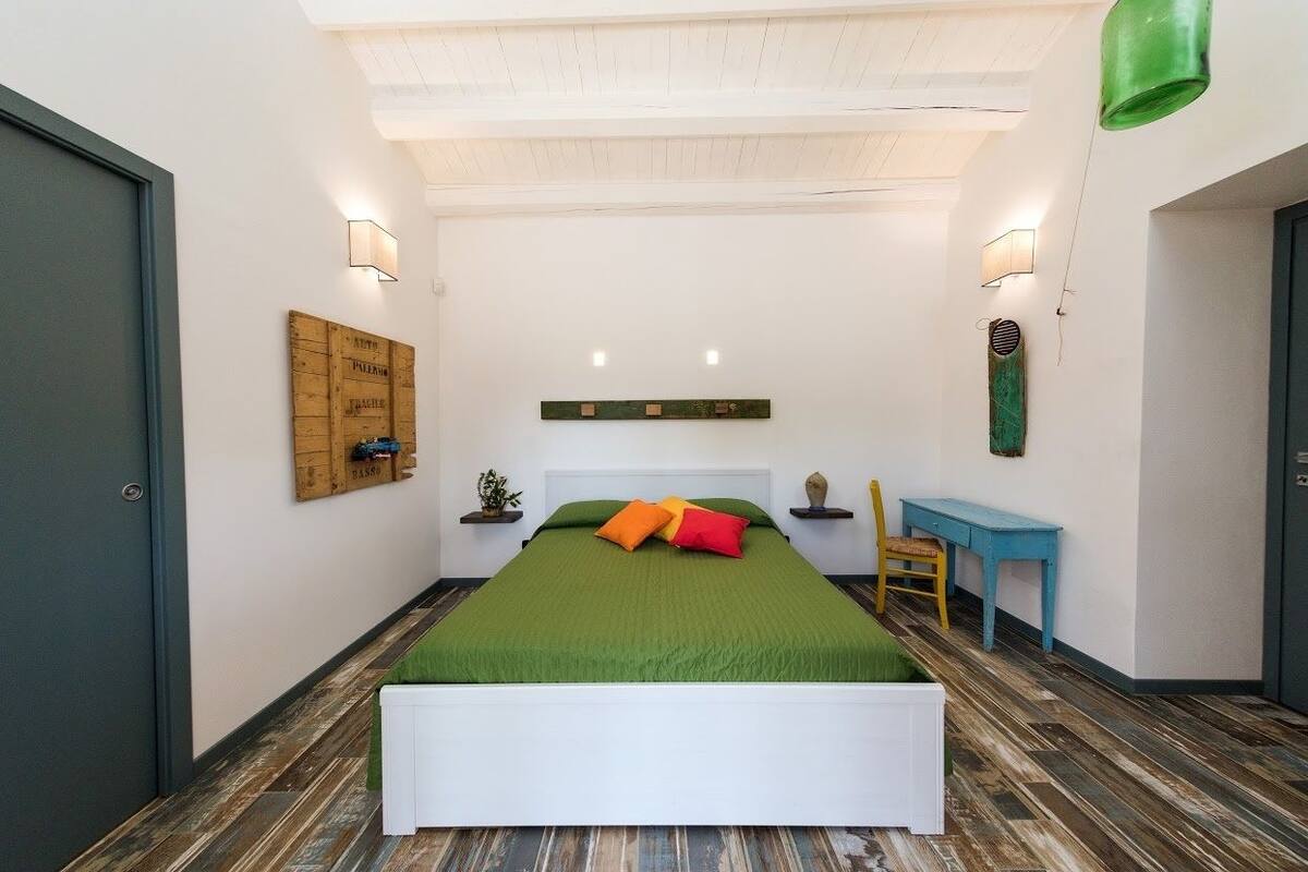 Un dormitorio con una cama grande, cabecera de madera, colcha verde y un escritorio pequeño con silla.