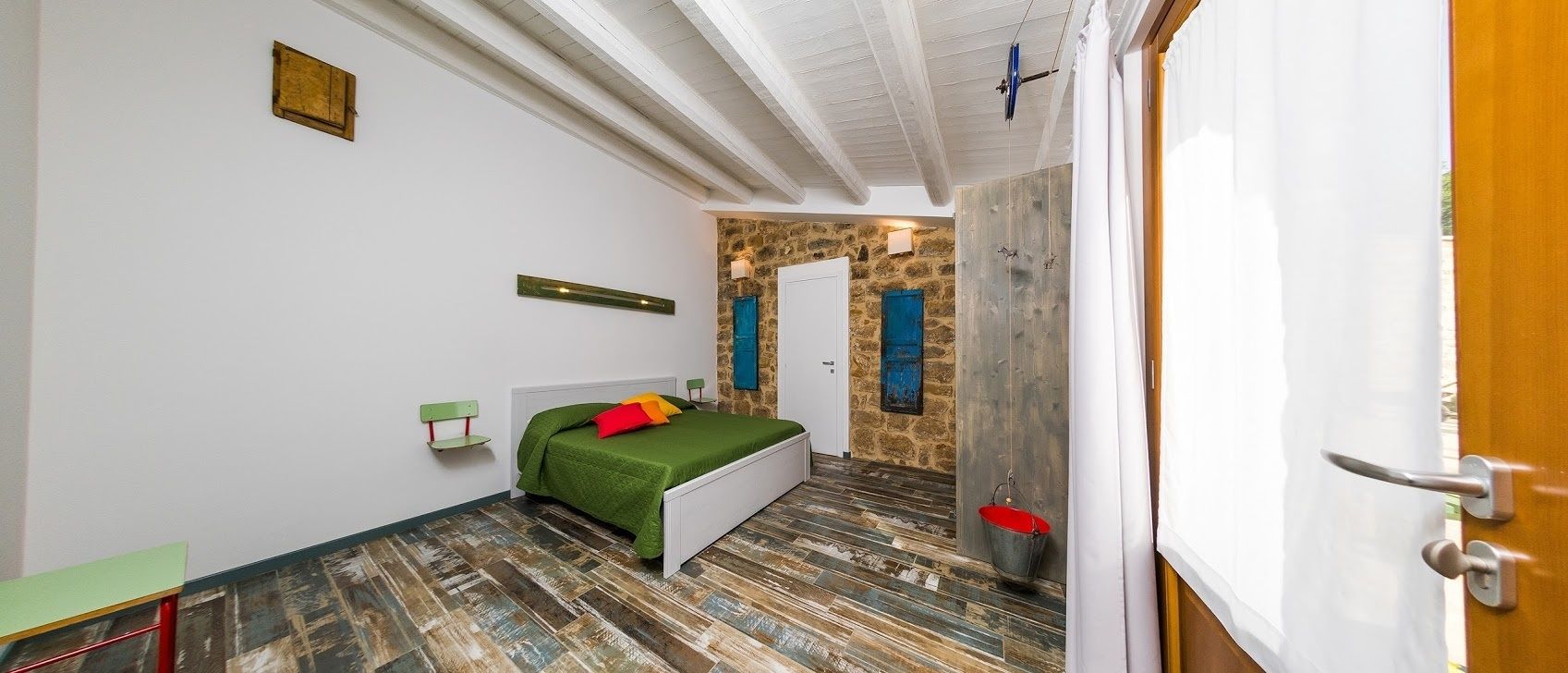 A bedroom with a bed, a wooden floor, a stone wall, and a door.
