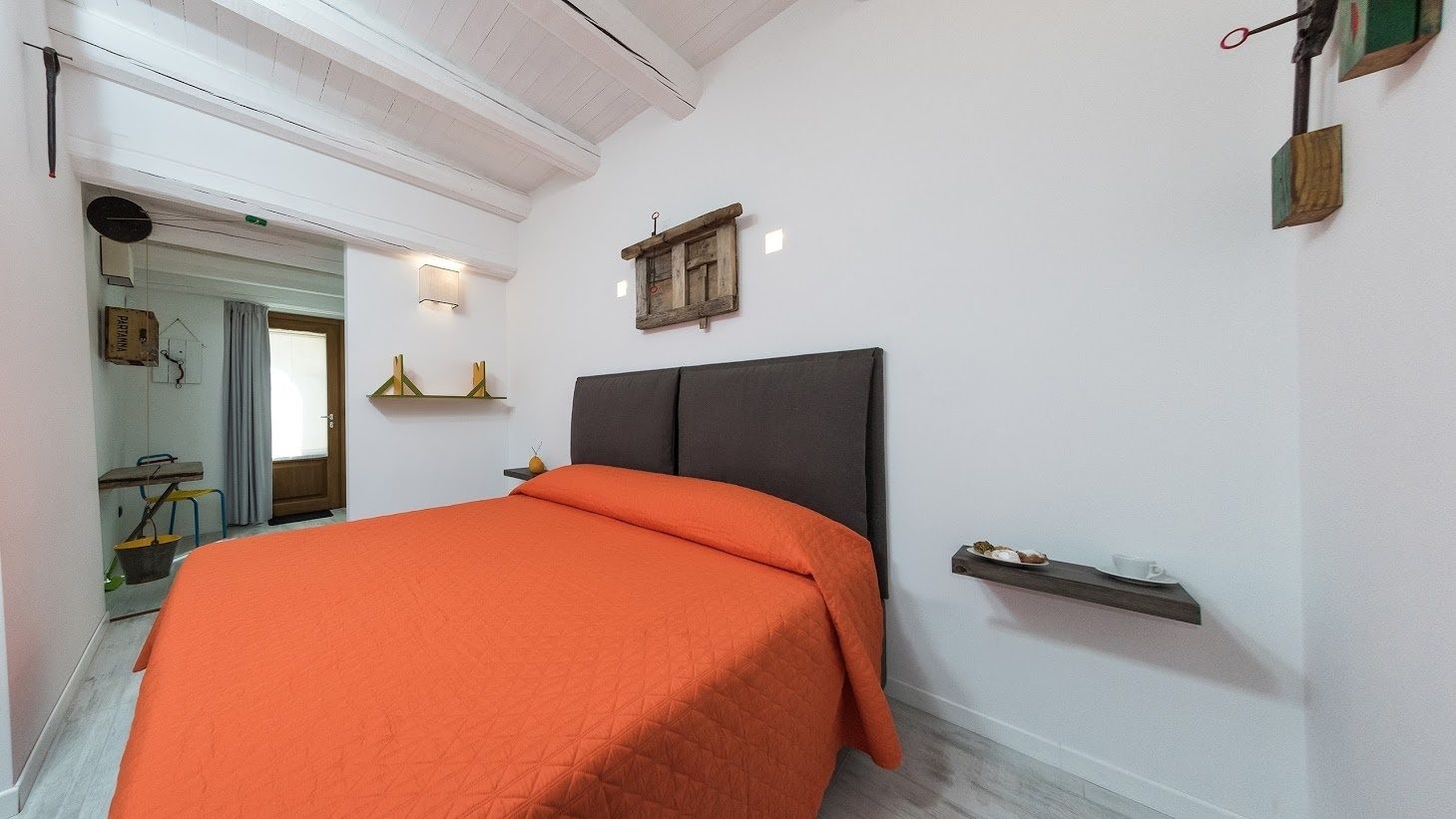Un dormitorio con una cama, un cabecero, un estante con una taza y un plato, y un espejo en la pared.