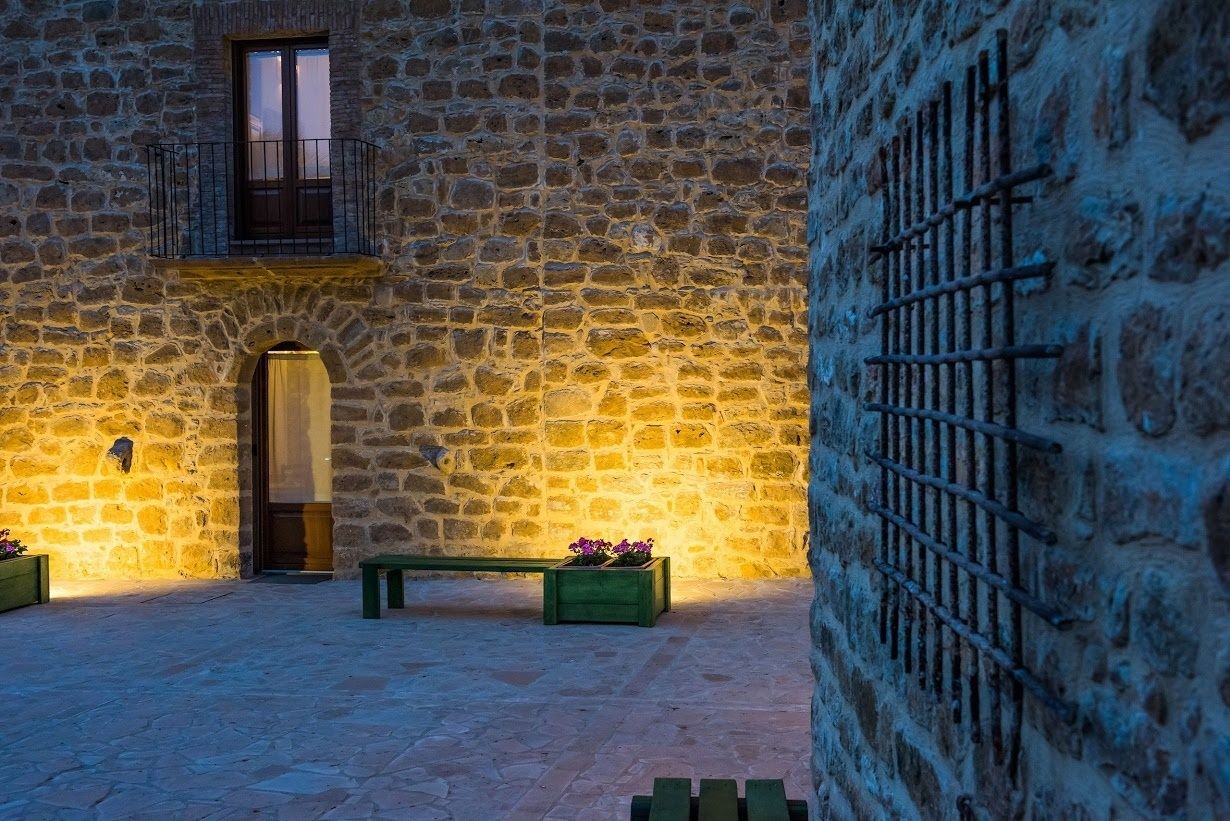 A stone courtyard with a wooden bench, a door, and a window with a balcony.