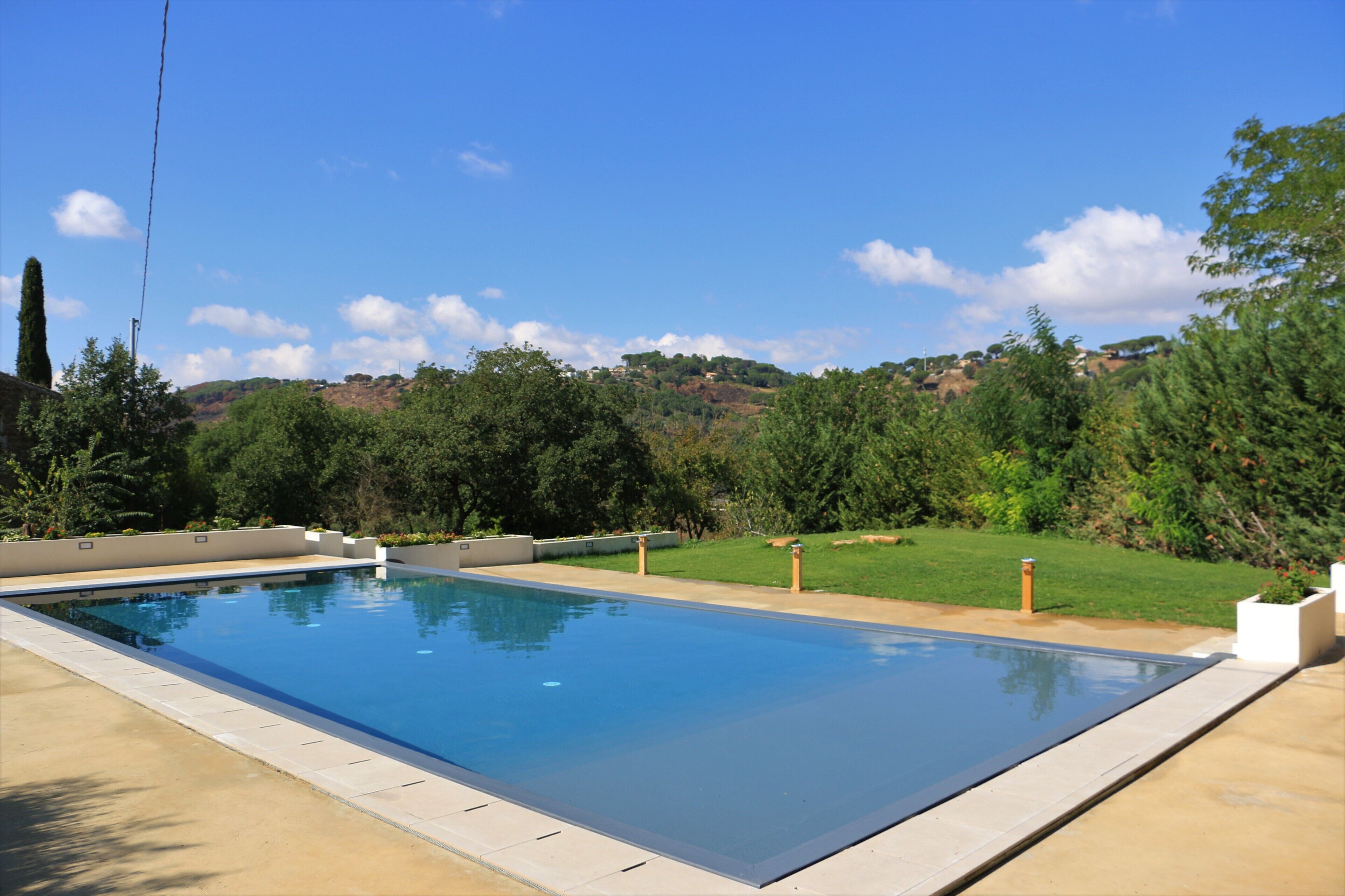 A rectangular swimming pool with a clear blue water surface, surrounded by a concrete deck and bordered by a low wall.