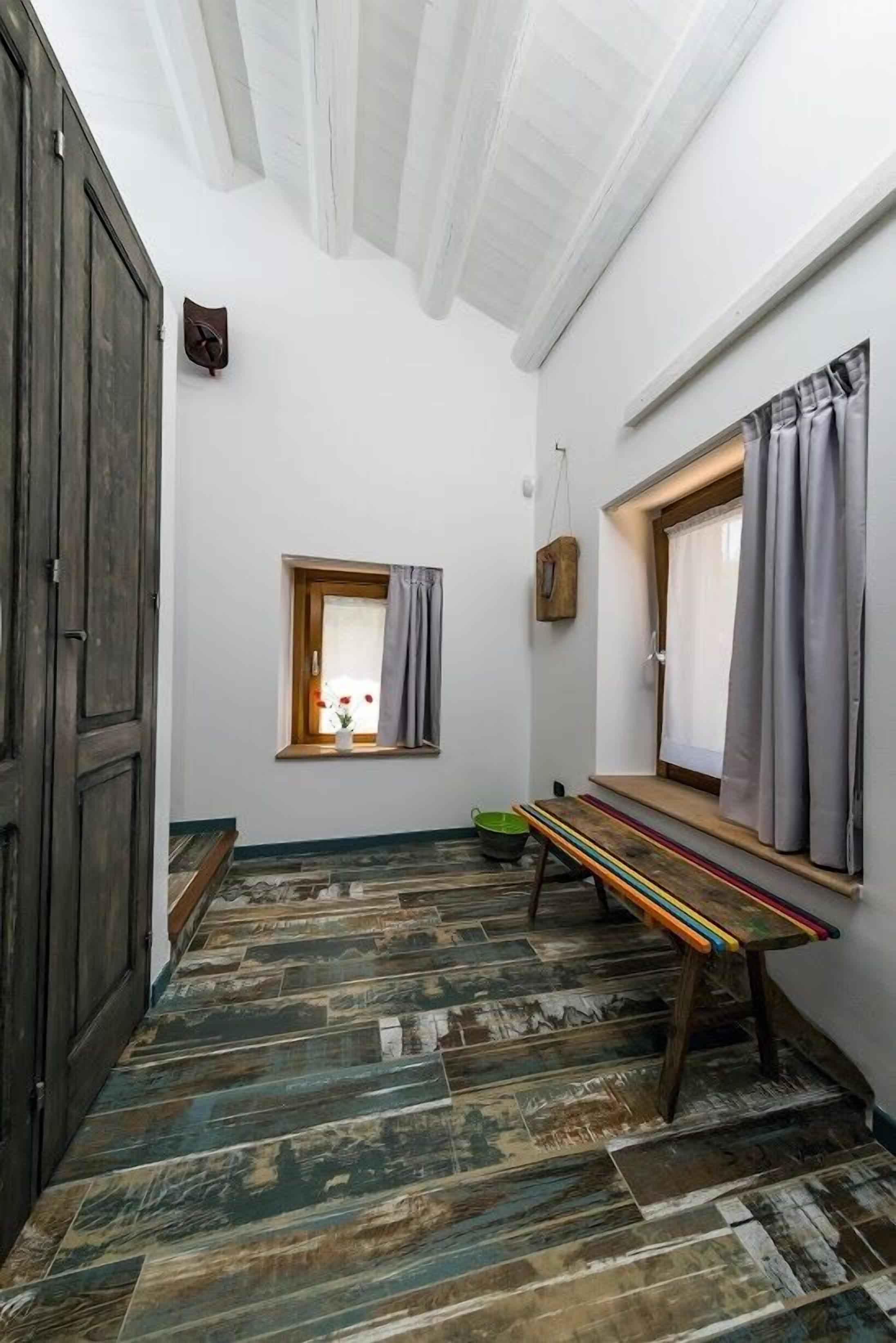 A narrow hallway with a wooden bench, a small window with curtains, and a wall-mounted light fixture.