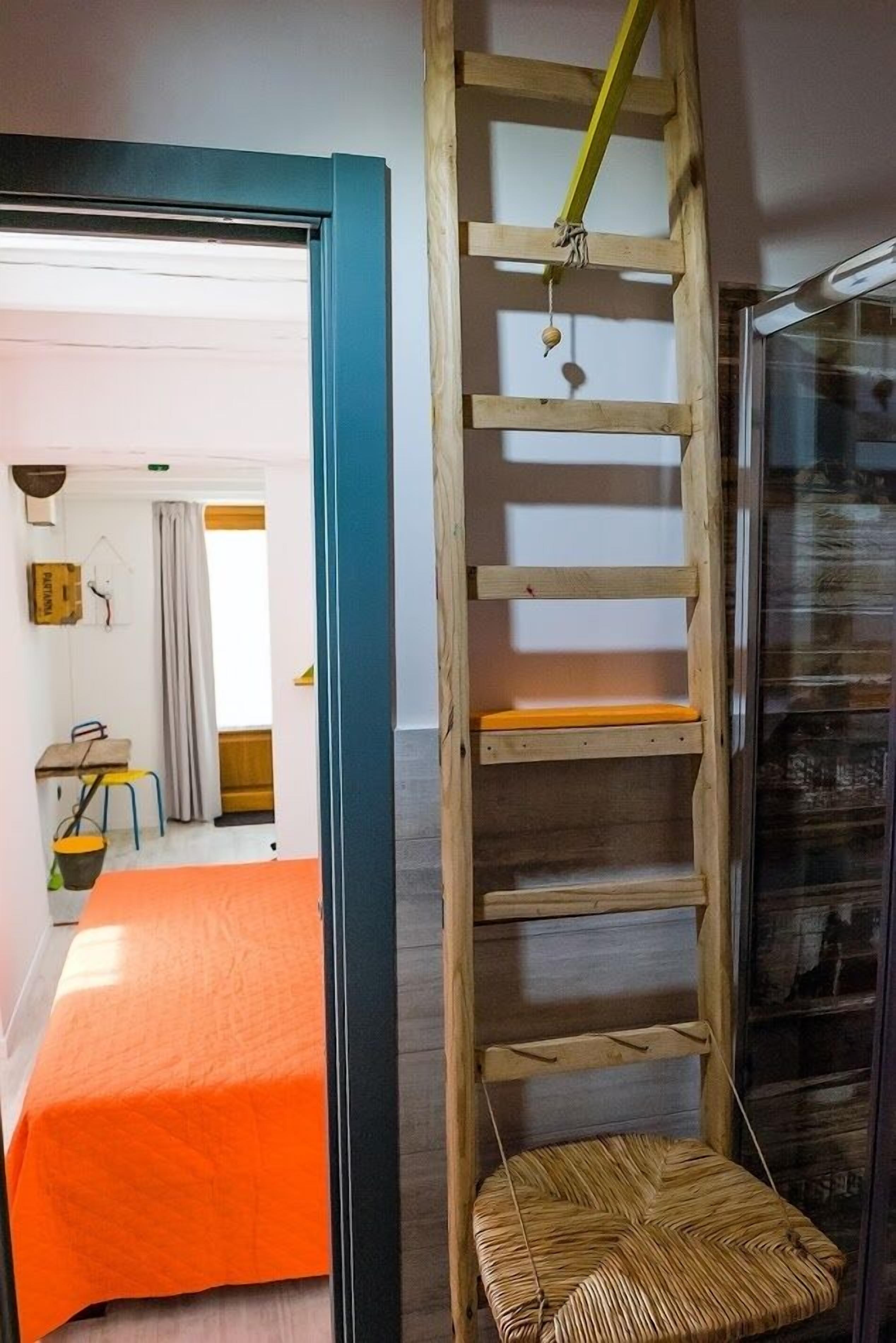 A room with a wooden ladder, a wicker chair, and a bed with an orange bedspread.
