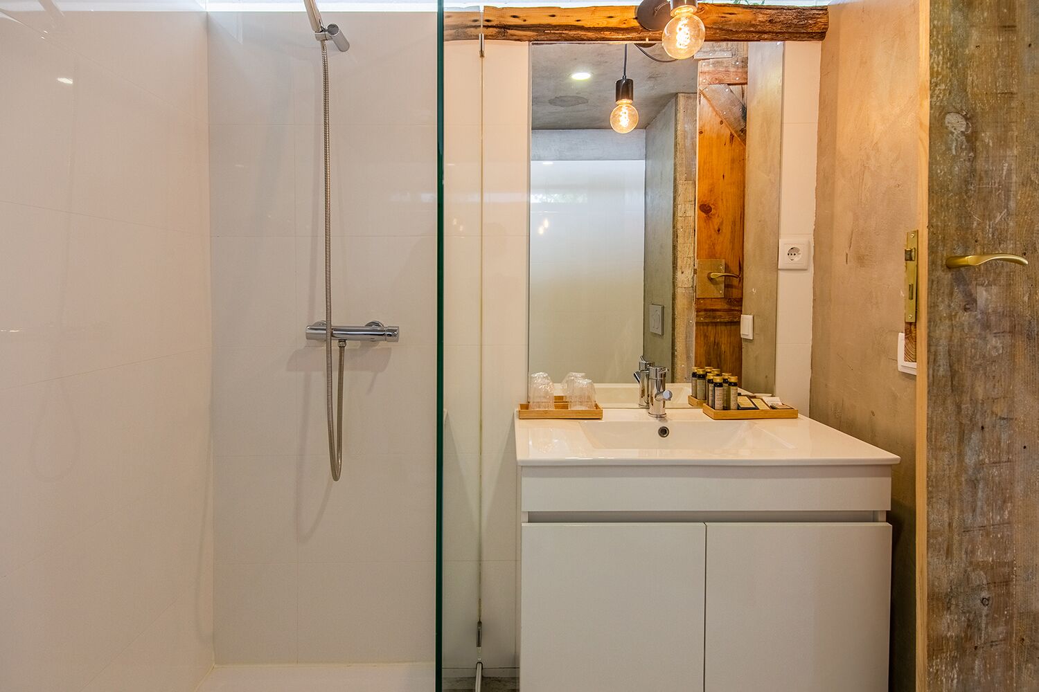 Ein Badezimmer mit einer gläsernen Duschkabine, einem weißen Waschbecken mit Spiegel und Holzelementen.