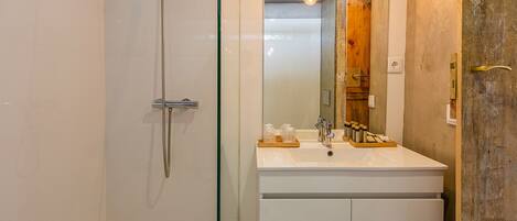 A bathroom with a glass-enclosed shower, a white sink with a mirror, and wooden accents.