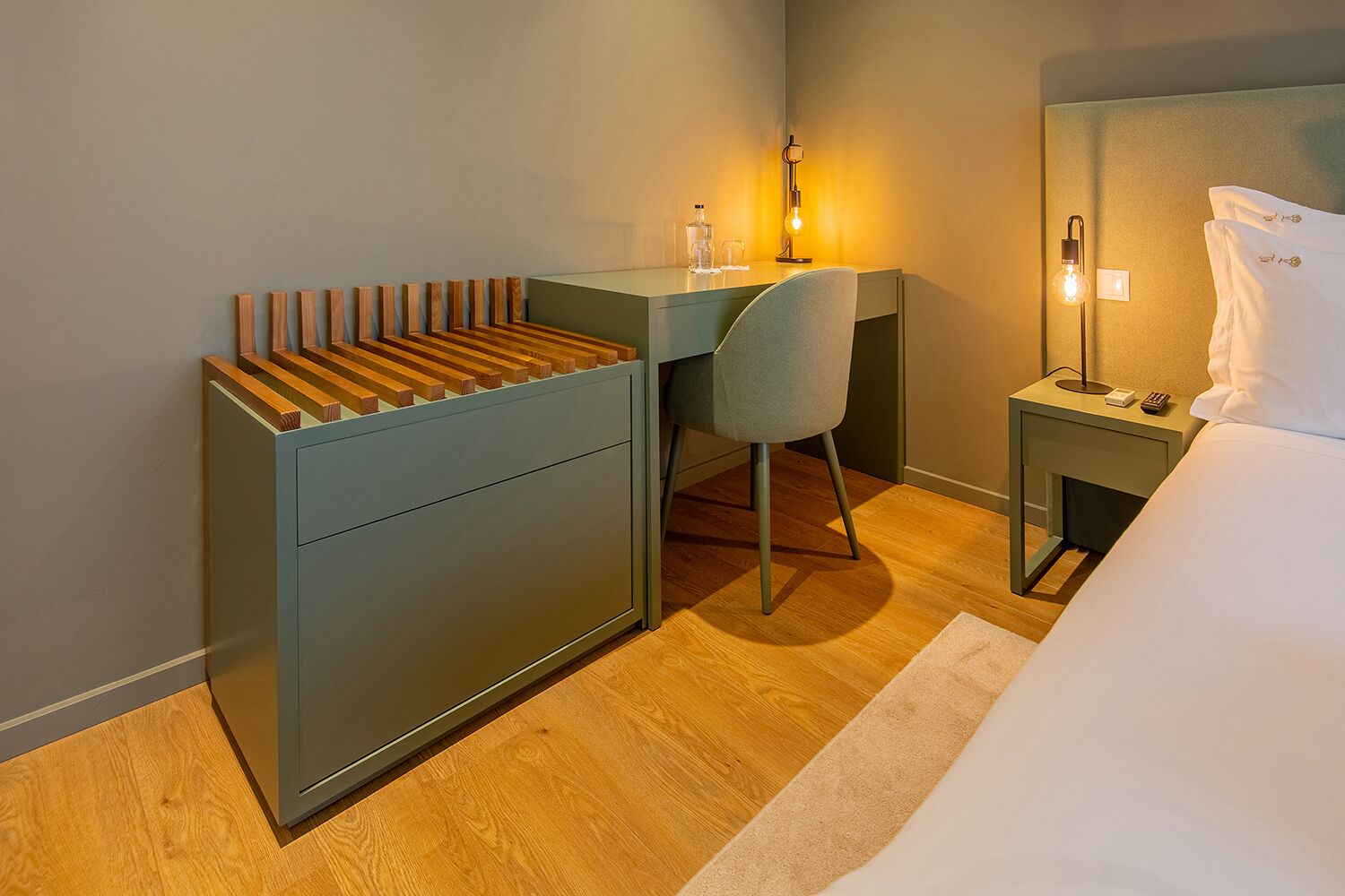 Una habitación de hotel con escritorio, silla, mesita de noche, lámpara y cama.