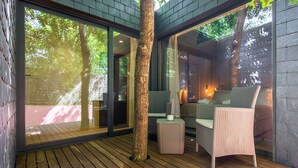 Uma área de estar moderna ao ar livre, com móveis de vime, um deck de madeira e grandes portas de vidro que dão para um ambiente interno.