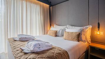 Quarto de hotel com cama, duas almofadas, mesa de cabeceira, abajur e janela com cortinas.