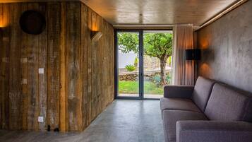 A modern interior with a wooden accent wall, a grey sofa, and a large sliding glass door leading to an outdoor garden.