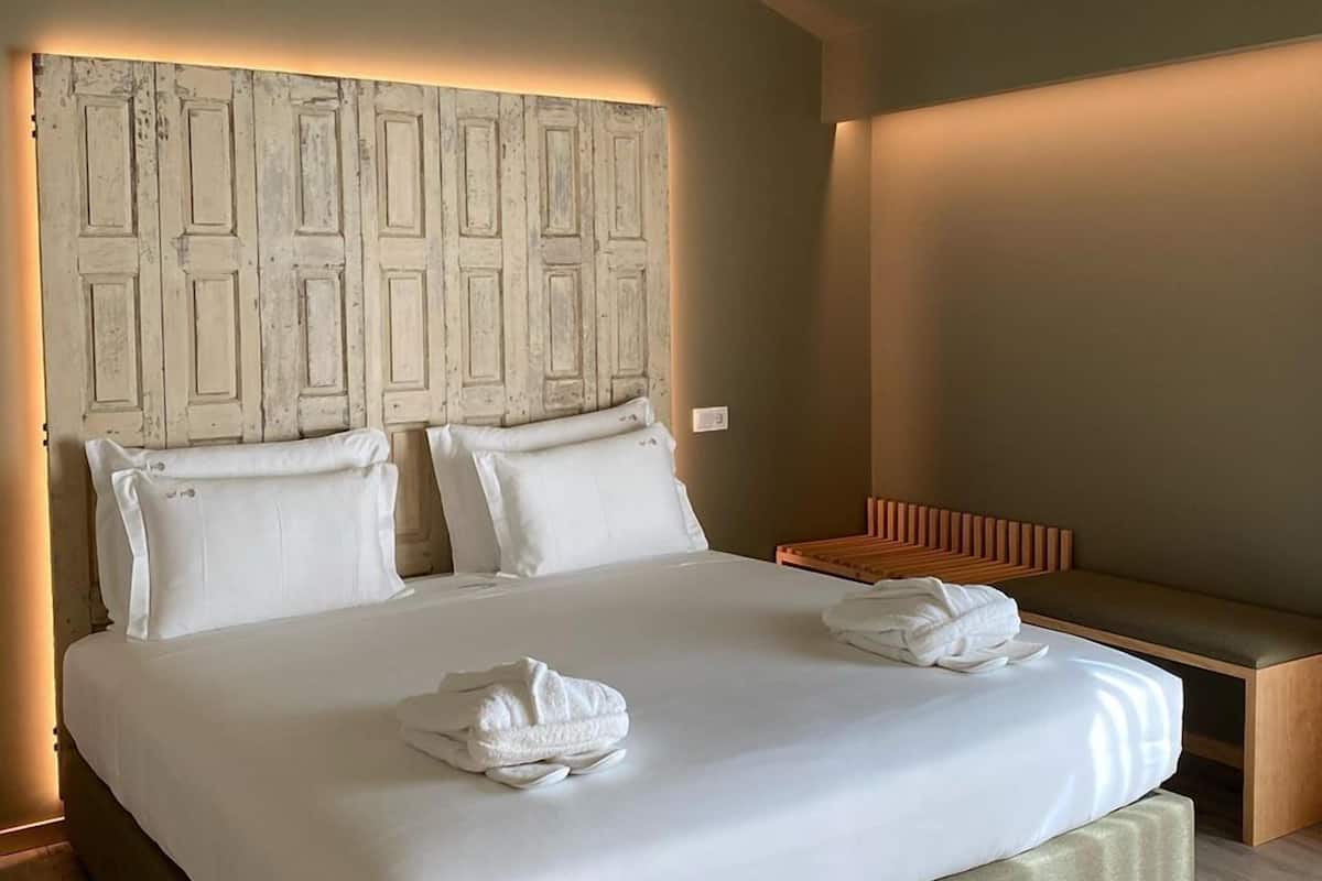 Une chambre d’hôtel avec un grand lit, deux oreillers, une table de chevet avec une serviette et un banc.