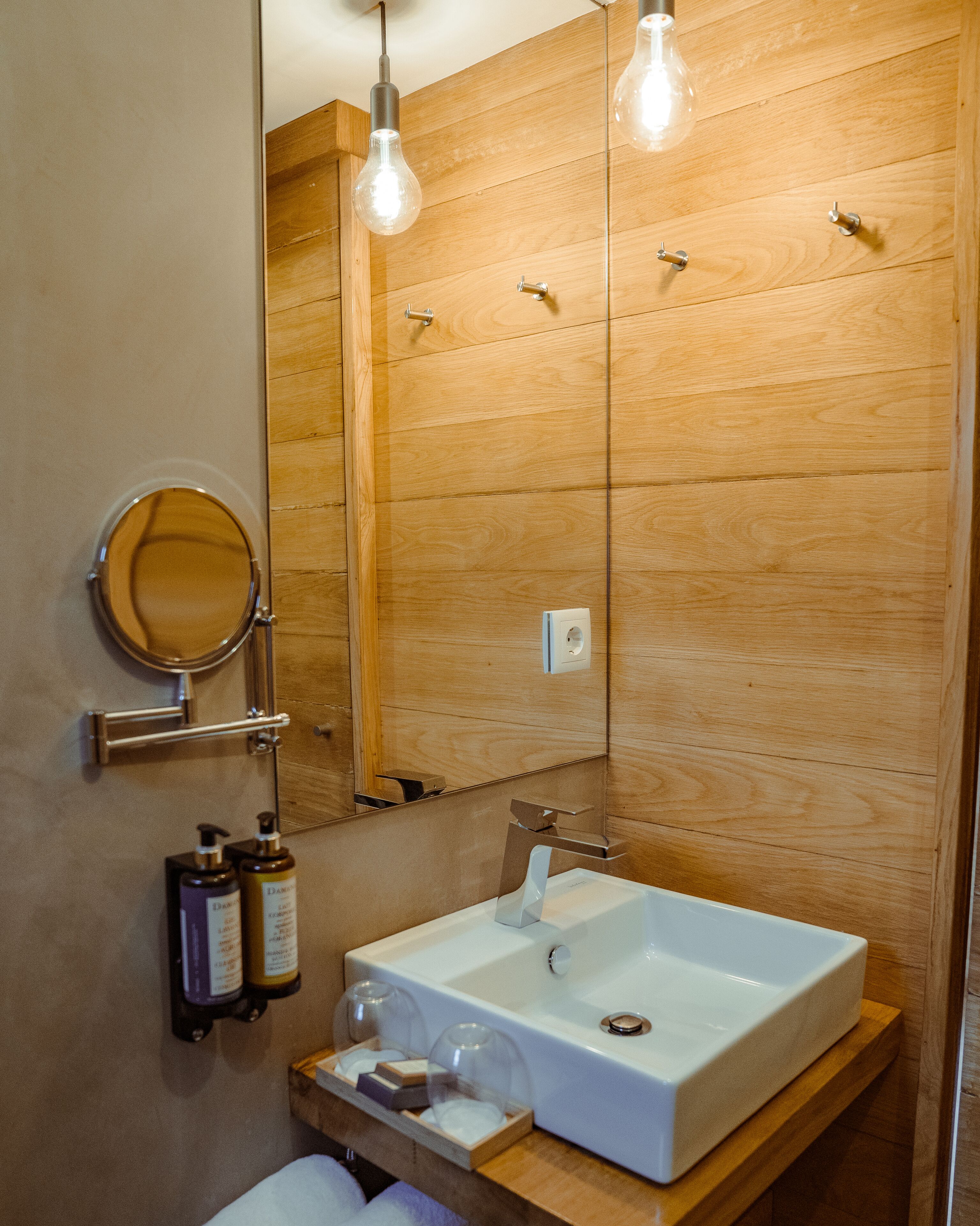 A bathroom with a wooden vanity, a white sink, a mirror, and two bottles of shampoo.
