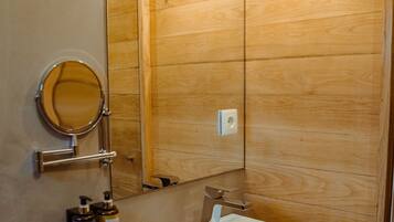 A bathroom with a wooden vanity, a white sink, a mirror, and two bottles of shampoo.