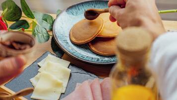 Desayuno con tortitas, queso, jamón y una botella de zumo de naranja sobre una mesa de madera.
