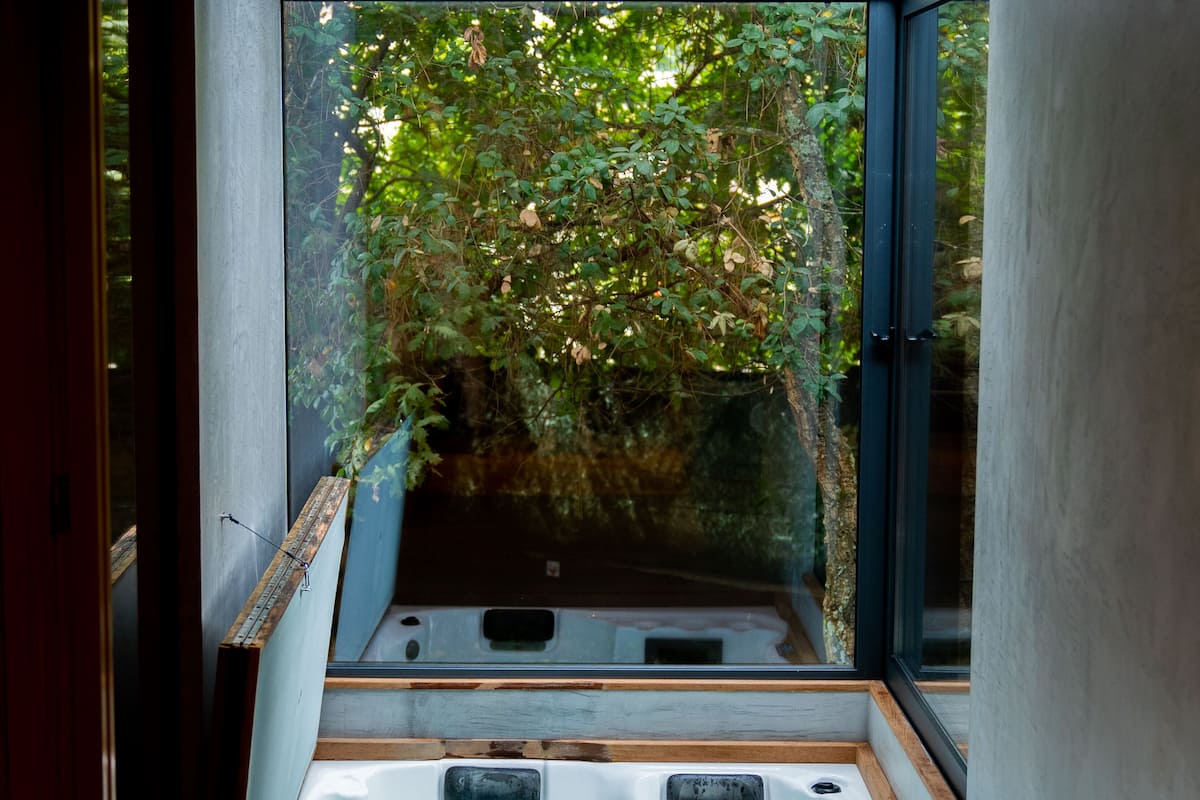 Une salle de spa moderne dotée d’une grande fenêtre, d’un jacuzzi et d’un banc en bois.