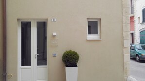 A beige building with a white door, a small window, and a potted plant. - Vicolo Fiore Affittacamere (Matera)