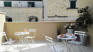 A small outdoor dining area with a table and chairs, a potted plant, and a view of buildings in the background. - Vicolo Fiore Affittacamere (Matera)