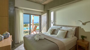 Un dormitorio con una cama grande, una mesita de noche de madera, vista al mar y un balcón con una silla.