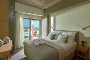 A bedroom with a large bed, a wooden nightstand, a view of the sea, and a balcony with a chair. - Villa GG (Hersonissos)