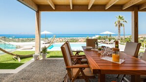 Terraza de madera con mesa lista para comer, con vista a una piscina y al océano.