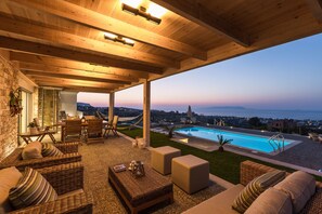 A covered outdoor seating area with wicker furniture, a pool, and a view of the sea.