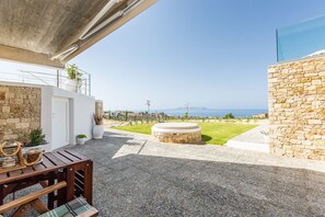 A patio with a view of the sea, a round stone table, and a wooden bench. - Villa GG (Hersonissos)