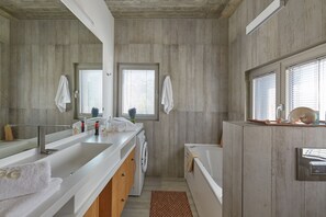 A modern bathroom with a large mirror, a built-in washing machine, and a bathtub. - Villa GG (Hersonissos)