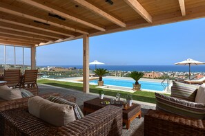 A covered outdoor seating area with wicker furniture, a pool, and a view of the sea. - Villa GG (Hersonissos)