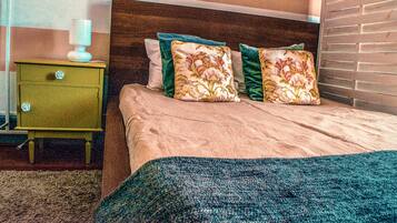 A bed with floral pillows, a green nightstand with a lamp, and a brick wall.