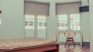 Une pièce avec un lit, une chaise, de grandes fenêtres et un téléviseur.