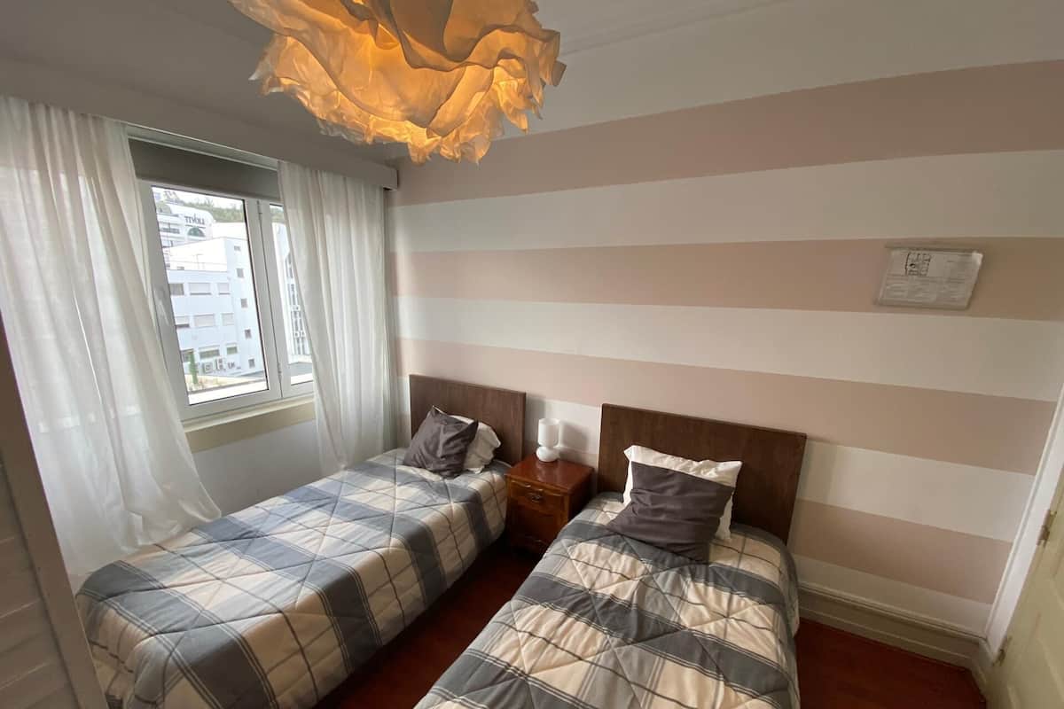 Ein Hotelzimmer mit zwei Betten, einem Fenster mit Vorhängen, einem hölzernen Kopfteil und einer wandmontierten Leuchte.