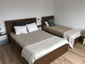 Een tweepersoonsbed met een houten hoofdbord en een witte deken. Er staat een nachtkastje met een lamp en een klein tafeltje naast het bed.