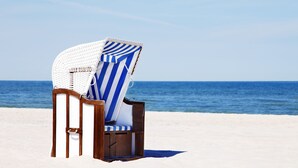 A beach chair with a striped cover on a sandy beach with a view of the ocean. - Strandkind - Dein Ostseehotel (Neustadt in Holstein)