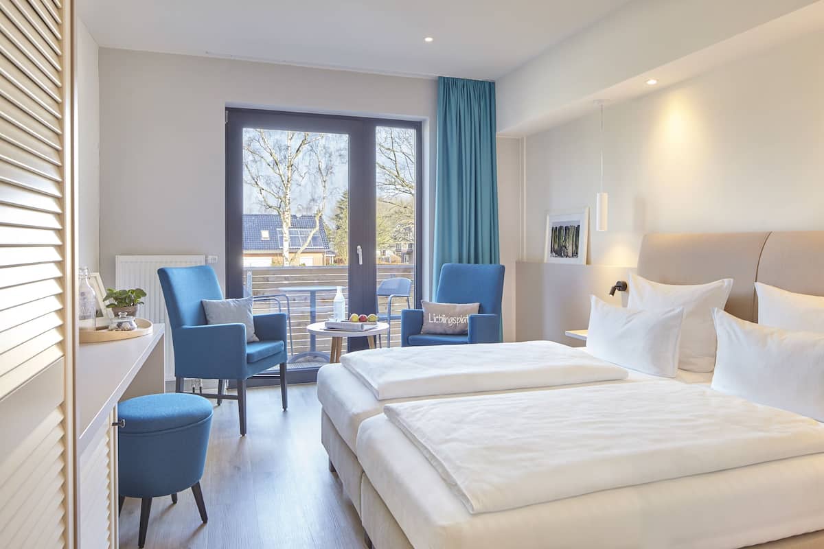 A hotel room with a large bed, two armchairs, a small table, and a view of the outside.
