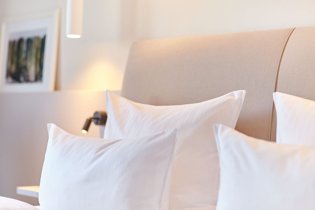 A neatly made bed with white pillows and a beige headboard.