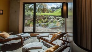 A spa room with three wooden loungers, a large window with a view of a garden, and a hanging light fixture. - Strandkind - Dein Ostseehotel (Neustadt in Holstein)