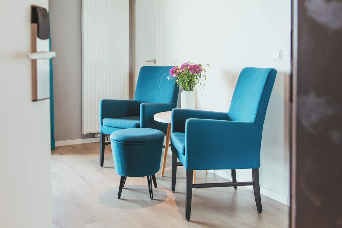 A modern room with two blue armchairs, a small round table, and a vase with flowers.