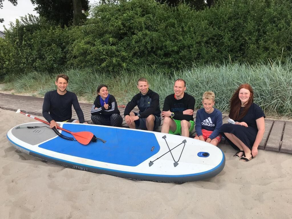 A group of people sitting on a beach with a paddleboard in front of them.