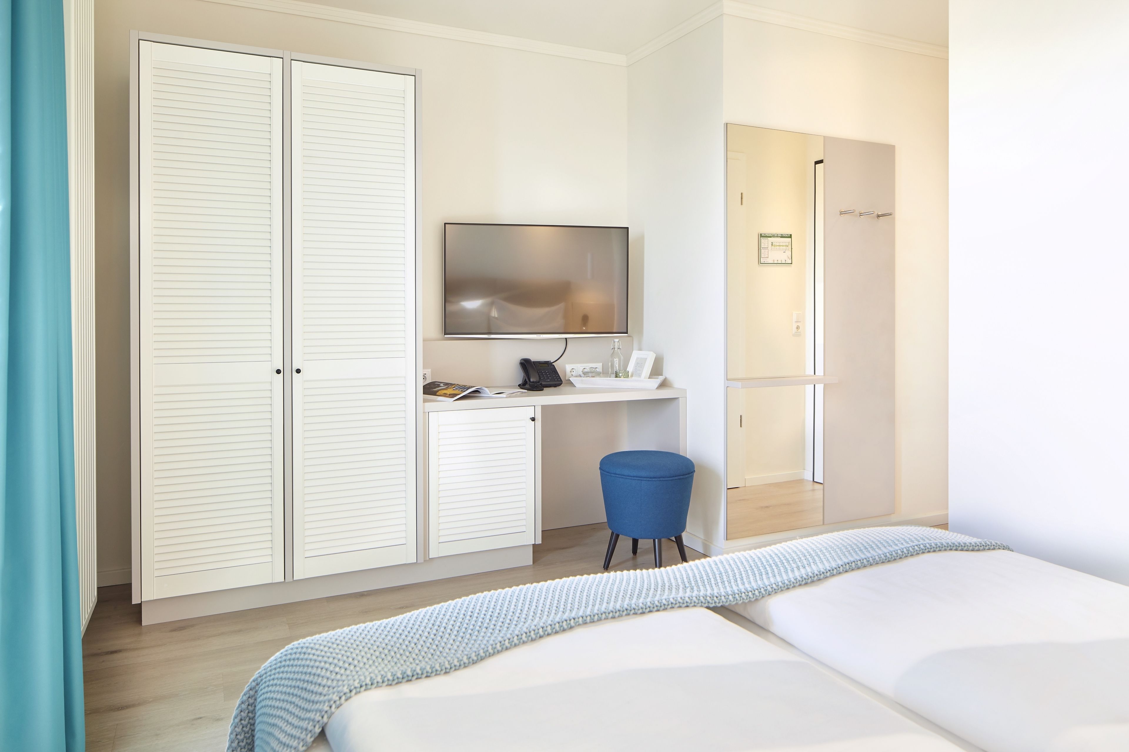 A hotel room with a bed, a desk with a computer, a TV, and a wardrobe.
