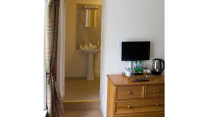 Ein Badezimmer mit Waschbecken, Spiegel und Toilette. Ein Holzkonsolenmöbel trägt einen Fernseher und einen Wasserkocher.