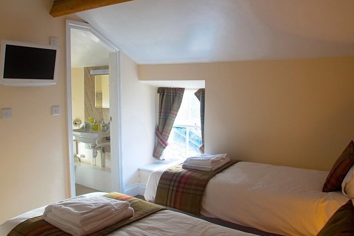 A bedroom with two beds, a television, and a bathroom visible through an open door.