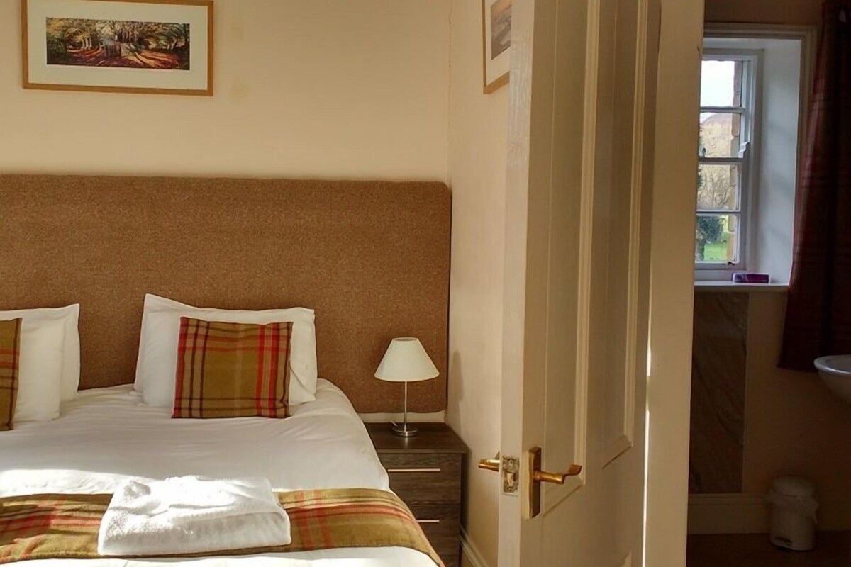 A hotel room with a bed, a nightstand, a lamp, and a door leading to a bathroom.